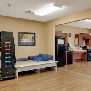 A view of a home interior featuring a living area with exercise equipment and an adjacent kitchen.