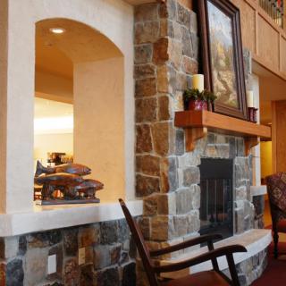 A cozy living room interior featuring a stone fireplace with a wooden mantel, adorned with candles and artwork.