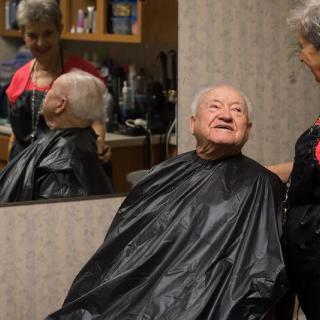 An elderly man smiles while getting a haircut in a salon.