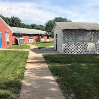 A peaceful pathway through a landscape of red brick buildings and green grass.