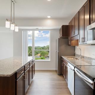 A modern kitchen with dark wood cabinets, granite countertops, and stainless steel appliances, featuring a large window with a scenic view.