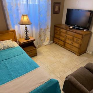 A cozy bedroom setup featuring a bed with turquoise bedding, a lamp, a TV, and a wooden dresser.