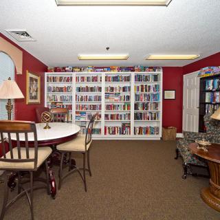 A cozy library room featuring bookshelves filled with books, a round table with chairs, and warm lighting.