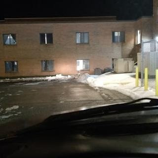A view of a building at night, with snow on the ground and parked vehicles.