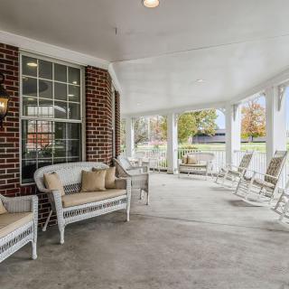 A cozy porch with rocking chairs and cushioned seating against a brick wall.