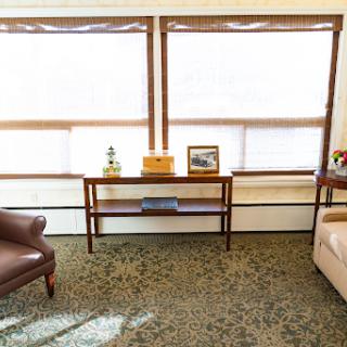A cozy living room featuring a brown armchair, beige sofa, and a coffee table positioned near large windows that let in plenty of natural light.