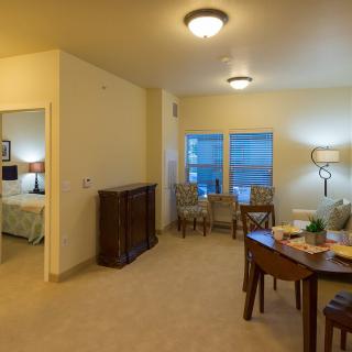A cozy living room and dining area with adjoining bedroom, featuring stylish furniture and ample lighting.