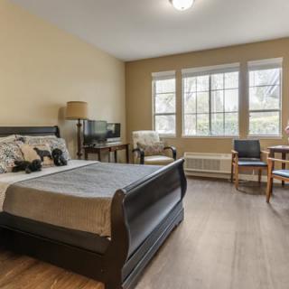 A cozy bedroom with a large bed, seating area, and natural light from big windows.