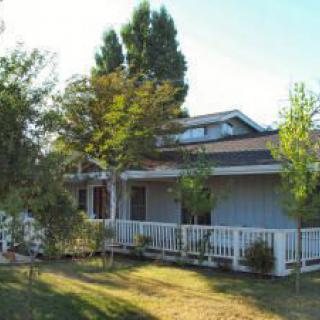 A charming house with a large porch surrounded by lush trees and a well-maintained yard.