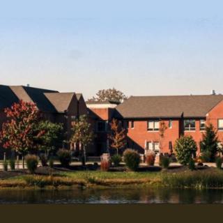 A scenic view of brick residential buildings by a pond, surrounded by trees.
