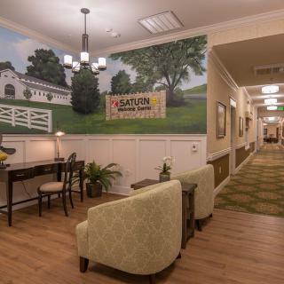 A cozy lobby area with a seating arrangement, featuring a landscape wall mural and a desk.