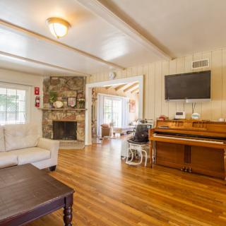 A cozy living room with a piano, stone fireplace, and hardwood floors.