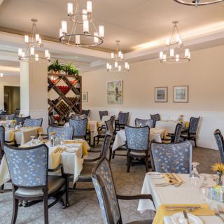 A spacious and elegantly decorated restaurant dining area with neatly arranged tables and chandeliers hanging from the ceiling.