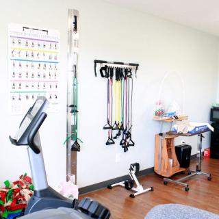 A rehabilitation room equipped with various gym equipment including an exercise bike and resistance bands.