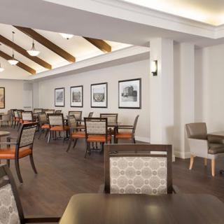 A modern dining room with neatly arranged tables and chairs, decorated with framed pictures and wooden ceiling beams.