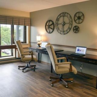 A modern office space with two desks and chairs, featuring wall decor and natural light from large windows.