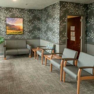 A calm and neatly arranged waiting room with multiple chairs, a painting on the wall, and patterned wallpaper.
