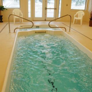 Cozy indoor swimming spa with chairs and handrails.