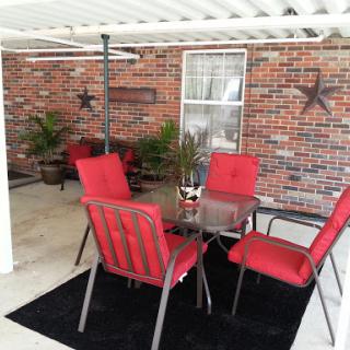 A cozy outdoor patio setup featuring a glass table surrounded by red chairs and decorative plants.