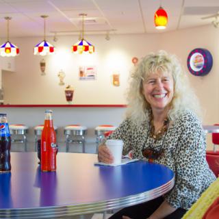 A smiling woman enjoying a drink in a retro-themed diner.