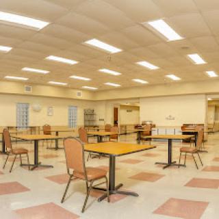 A spacious, empty room with tables and chairs, illuminated by bright overhead lights.