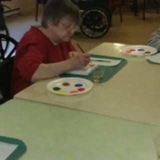 A senior person engaged in painting at a table with an art palette.