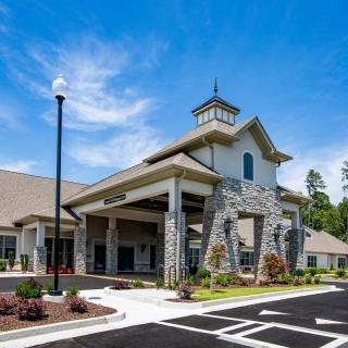 A modern building with a stone facade and landscaped entrance under a clear blue sky.