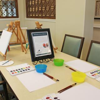 A table set up for an art class with easels, paint palettes, brushes, and paper.