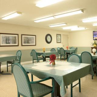 A spacious dining area featuring green tables and chairs, illuminated by overhead lighting.