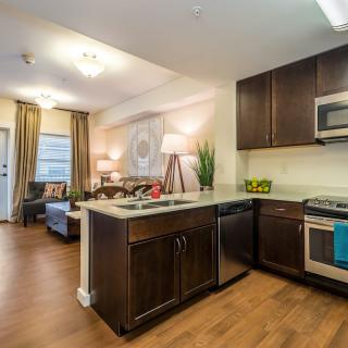 A modern open concept kitchen and living area with wood flooring and stainless steel appliances.