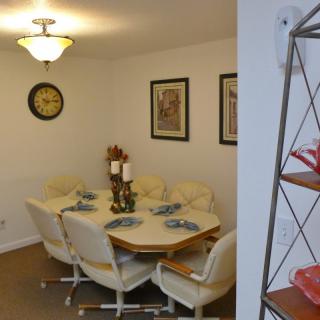 A cozy dining room featuring a set of six chairs around a wooden table, decorated with placemats and candles, complemented by wall art and a clock.
