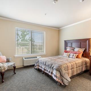 A cozy bedroom with a neatly made bed, an armchair, and a large window providing natural light.