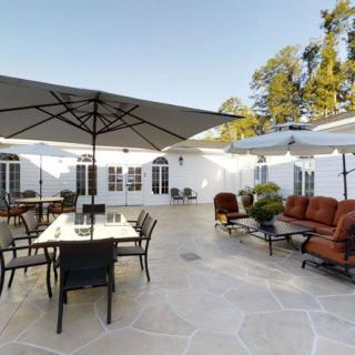 A spacious patio with outdoor furniture including tables, chairs, and large umbrellas on a sunny day.