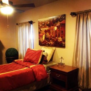 A cozy bedroom with elegant decor, featuring a bed with red bedding, framed artwork on the wall, and a wooden nightstand.