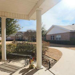 A sunny day view of a porch with a bench, overlooking a pathway and residential buildings.