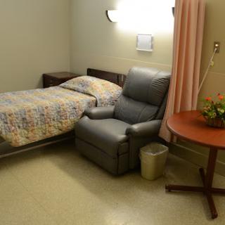 A serene hospital room featuring a bed, a recliner chair, and a small table with flowers.