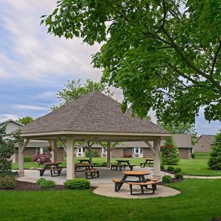 A serene park setting featuring a gazebo surrounded by picnic tables and lush greenery.