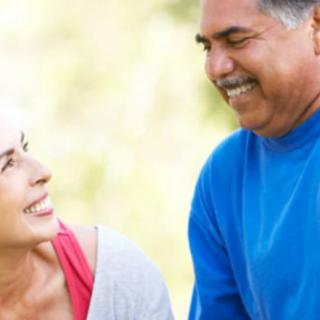 An elderly couple smiling and talking outdoors.