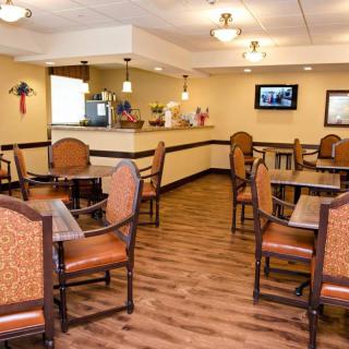 A cozy dining area featuring several tables and chairs, with warm lighting and a television on the wall.