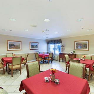 A cozy dining room with red tablecloths and neatly arranged tables and chairs, adorned with decorative paintings on the walls.