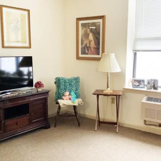 A cozy living room with a television, chair, and lamp, featuring artwork on the walls.