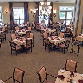 A spacious dining room with neatly arranged tables and chairs, featuring elegant chandeliers and large windows.