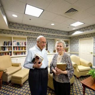 An elderly couple enjoying their time together in a cozy library setting, each holding a book.