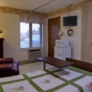 A cozy hotel room featuring a bed, small dresser, microwave, and refrigerator with a wall-mounted television.