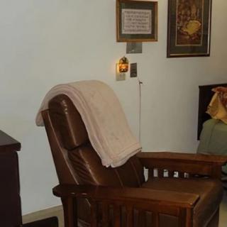 A cozy living room setup featuring a wooden chair with a blanket draped over the back, and decorative wall art.