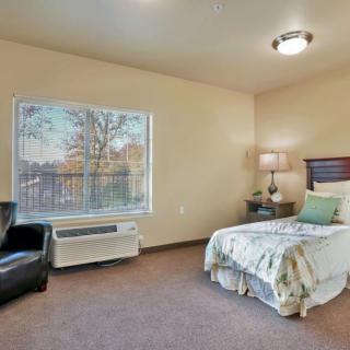 A cozy bedroom with a single bed, a lamp on the nightstand, and a large window.