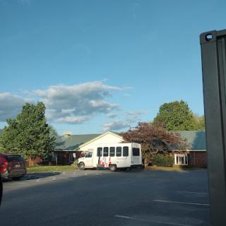 A view of a building with a parked vehicle against a backdrop of trees and a blue sky.