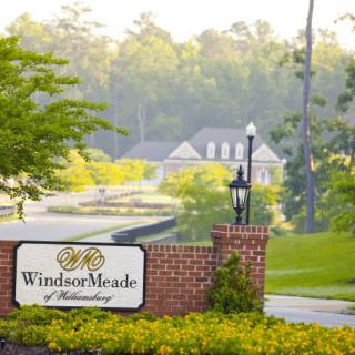 Entrance to the WindsorMeade of Williamsburg surrounded by lush greenery and a distant house.
