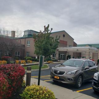 A view of a parking lot with cars in front of a large building, under a cloudy sky.