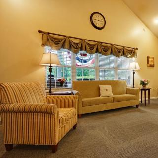 A cozy living room with a sofa and armchair, accented by table lamps and a wall clock.